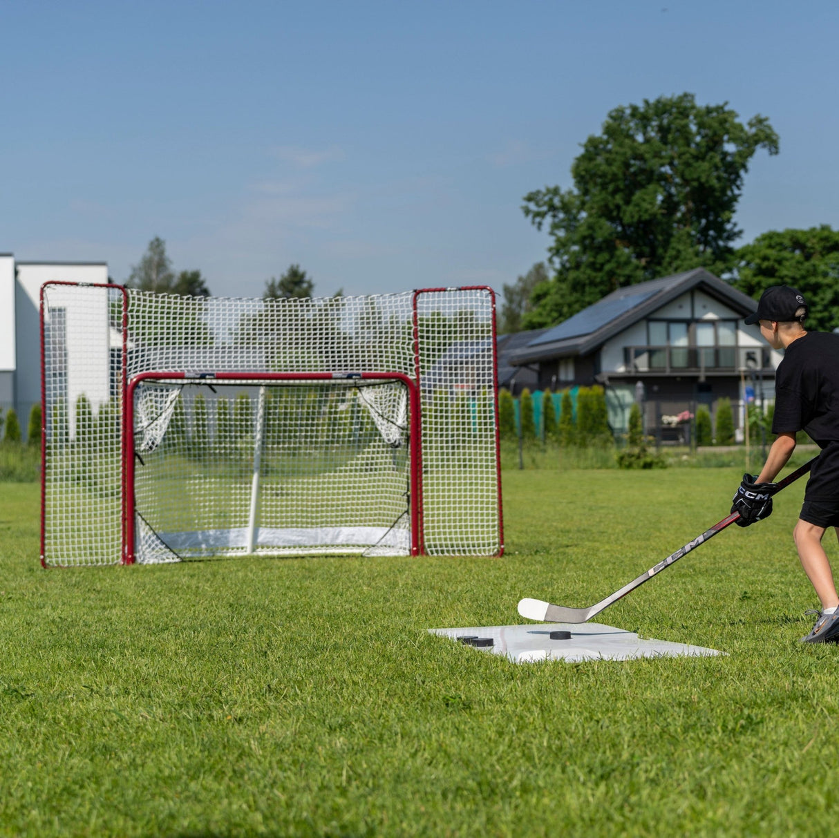 En spelare skjuter puckar mot ett hockeymål med backstop i gräsmatta, perfekt för hemmaträning och precision.