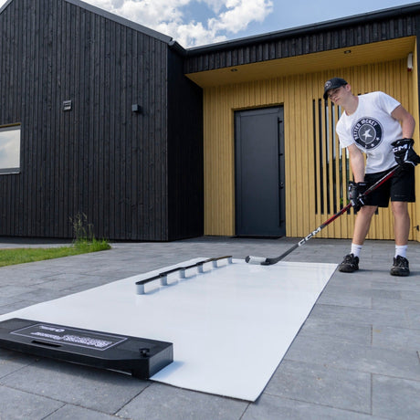 Hockeypassare för klubbteknik hockey, en spelare praktiserar passningar på en platt yta utanför ett modernt hus.