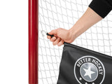 Hand attaching a Better Hockey target banner to a red goal net, enhancing practice for improved shooting precision.